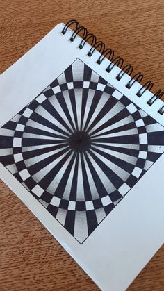 an open spiral notebook with black and white designs on the cover, sitting on a wooden table