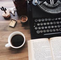 an old fashioned typewriter sitting on top of a table next to a cup of coffee