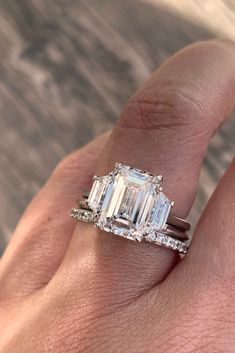 a woman's hand holding an emerald and diamond ring