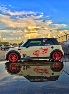 a small car with red rims is parked in front of a chain link fence