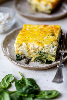 a slice of quiche with spinach and cheese on a plate next to silverware