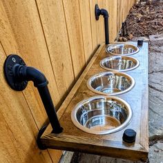 three metal bowls are lined up on a wooden shelf next to a wood fence and water faucet