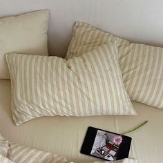 a cell phone sitting on top of a bed covered in pillows and blankets next to a flower