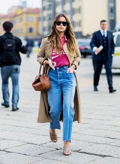 a woman walking down the street wearing high waist jeans and a trench coat with her hands in her pockets