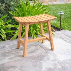 a wooden bench sitting on top of a cement ground next to green grass and bushes