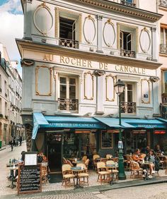 people are sitting at tables in front of a building with blue awnings on the street