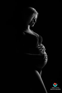 a pregnant woman standing in the dark with her hands on her stomach