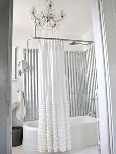 a white shower curtain in a bathroom next to a bathtub and sink with a chandelier