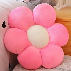 a pink flower shaped pillow sitting on top of a bed next to a white pillow