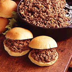 three sloppy joe sliders on a cutting board next to buns and bread rolls