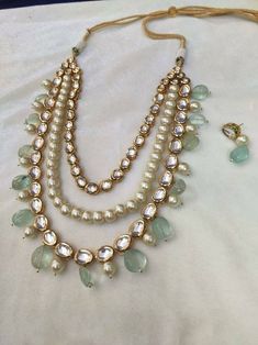 a necklace and earring set on a white cloth with pearls, beads and green stones