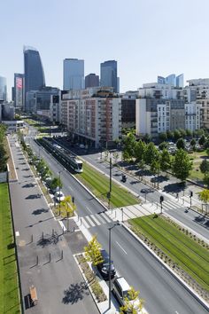 an aerial view of a city street with tall buildings in the background and green grass on both sides