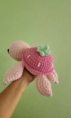 a pink crocheted turtle with a green bow on it's head is held by a hand