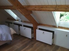 an attic bedroom with white storage cabinets and wood flooring, along with a bed in the corner