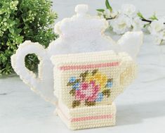 a teapot shaped like a cup with a lid and handle is sitting on a table next to some flowers