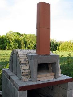 a brick oven sitting on top of a cement block in the middle of a field