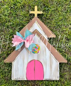 a wooden house with a pink door and a cross on the top is laying in the grass