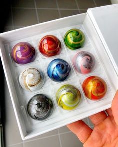 a person holding an open box filled with different colored marbles