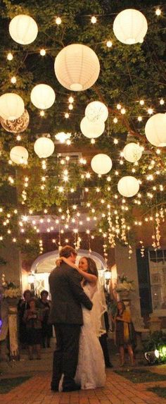 a bride and groom kissing under paper lanterns