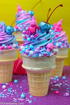 three ice cream cones topped with blue and pink sprinkles on a purple table