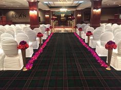 the aisle is lined with white chairs and pink flowers on each chair, along with black carpeted flooring