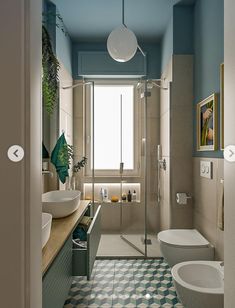 a bathroom with blue walls and tiled flooring, two sinks and a toilet in the corner