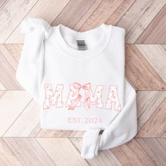 Custom Mama Sweatshirt, a charming blend of comfort and style that celebrates the elegance of ballet and the love of motherhood. Crafted with meticulous attention to detail, this tee is not just a garment but a statement piece for every proud ballet mom out there. The design features a delicate Coquette aesthetic with a blush pink floral font that spells out "MAMA." Adorned with a artfully tied pink ribbon, adding a whimsical touch to the design. Personalization is optional. If you choose to cus Personalized White Tops For Winter, White Sweatshirt For Mother's Day, White Tops For Birthday And Winter, White Top For Birthday In Winter, Cute White Sweatshirt For Mother's Day, Ballet Mom, Floral Font, Mom Crewneck, Personalized Ribbon