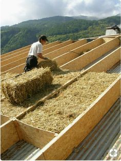 a man sitting on top of hay bales in the middle of a building with mountains in the background