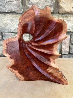 a wooden sculpture sitting on top of a table next to a stone wall with a brick wall in the background