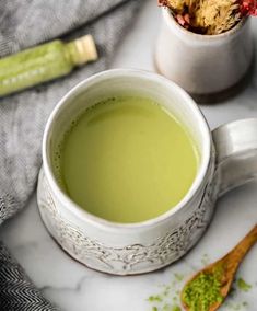 a cup of green tea next to a wooden spoon with some cookies in it on a marble surface