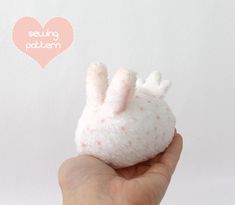 a hand holding a small white stuffed animal in it's right hand with a pink heart behind it