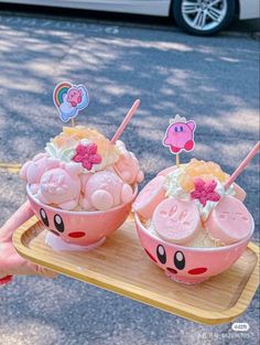 two pink bowls filled with ice cream on top of a wooden tray next to a white car