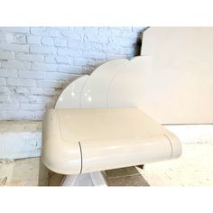 a white cloud shaped chair sitting in front of a brick wall on a tiled floor