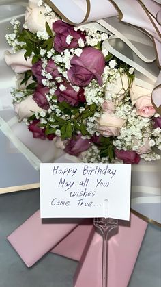 a bouquet of flowers sitting on top of a table next to a sign that says happy birthday may all your wishes come true