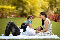 a woman, man and child laying on a blanket in the grass