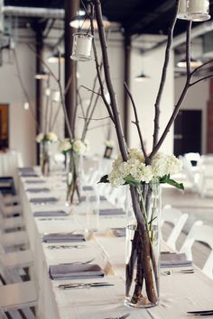 the table is set up with white flowers and branches in vases on each side