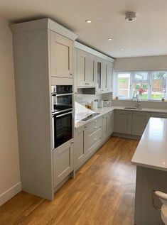 an empty kitchen with wooden floors and gray cabinets, white counter tops, and stainless steel appliances