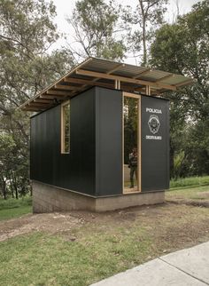 a small black building sitting on top of a lush green field next to a forest