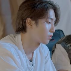 a young man sitting on top of a bed wearing a white shirt and silver necklace