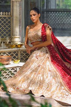 A gold tissue lehnga and choli features detailed zardoze and resham embroidery and is paired with a contrasting crimson cotton net dupatta adorned with gold zardoze borders and sequins. Gold Jamawar Dress With Dupatta, Elegant Jamawar Lehenga For Festive Occasions, Gold Embroidered Sharara For Reception, Anarkali Style Gold Lehenga With Intricate Embroidery, Gold Jamawar Sharara For Reception, Gold Saree Dress With Mirror Work, Gold Lehenga With Intricate Embroidery In Traditional Drape, Designer Tissue Silk Choli With Intricate Embroidery, Gold Jamawar Dress With Zari Work