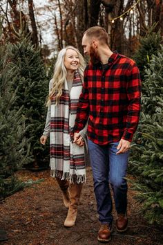 a man and woman walking through a christmas tree farm holding each other's hands