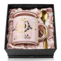 a pink coffee mug in a gift box with a gold spoon and fork next to it