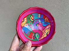 a hand holding a pink bowl with colorful designs on it