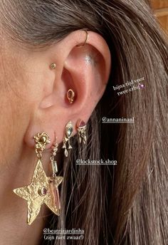 a close up of a person's ear wearing gold stars and danglings on them