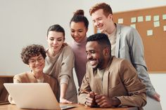 a group of people are looking at a laptop computer together in front of the camera