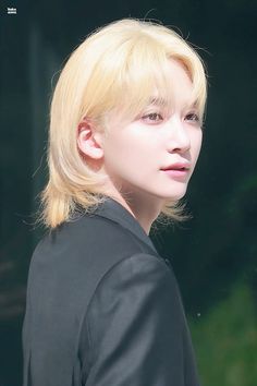 a young man with blonde hair wearing a black jacket and looking off into the distance