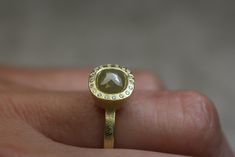 a close up of a person's hand holding a gold ring with a stone