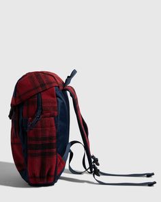 a red and black plaid backpack sitting on top of a white floor next to a wall