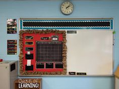 a bulletin board with writing on it next to a desk and a clock in the background