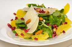 a white plate topped with spinach salad and orange slices covered in nuts, almonds and pomegranate